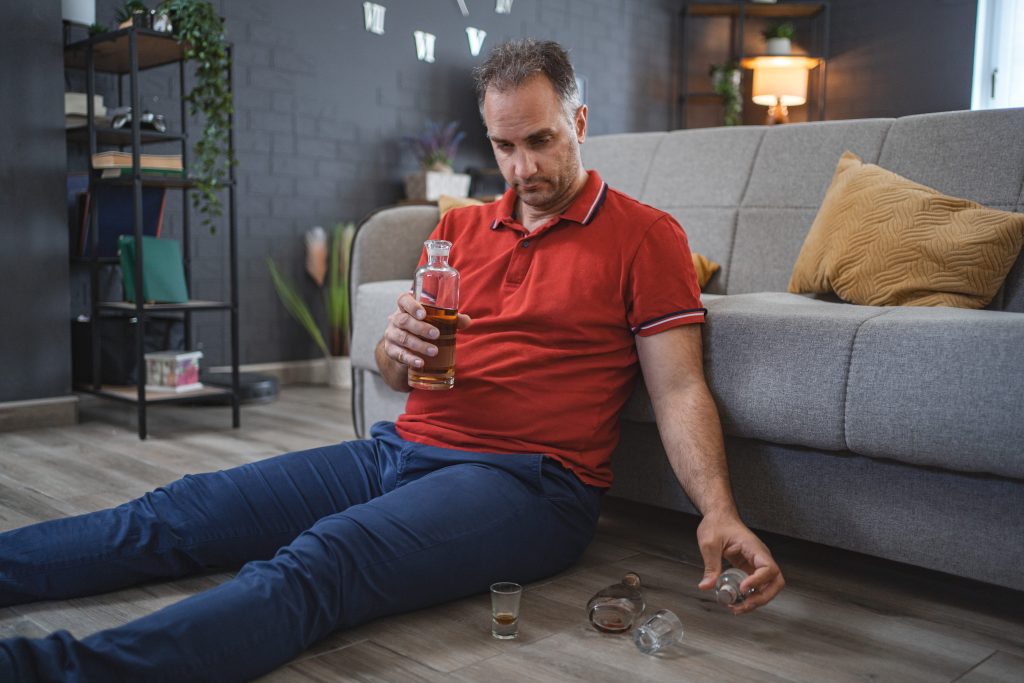 mężczyzna siedzący na podłodze i pijący alkohol